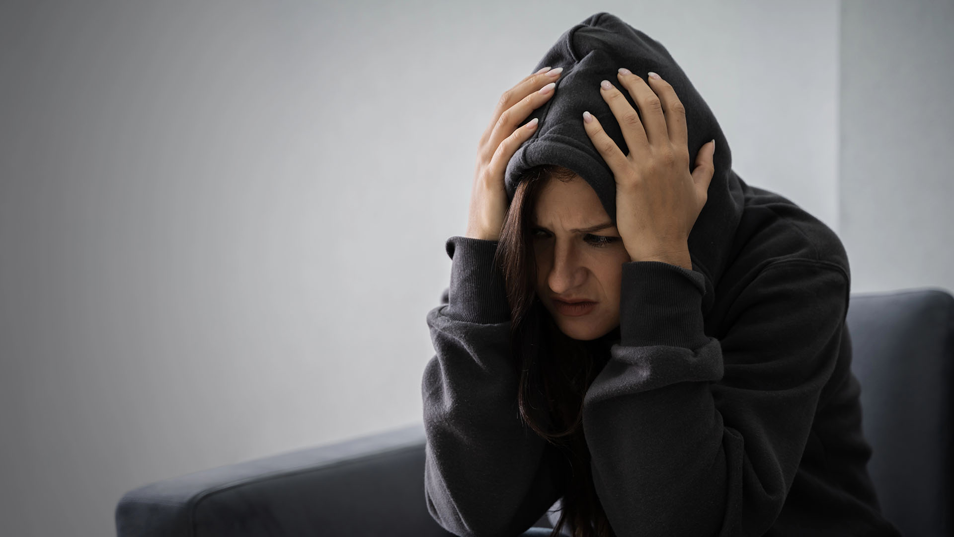 young depressed woman hoodie sitting sofa home