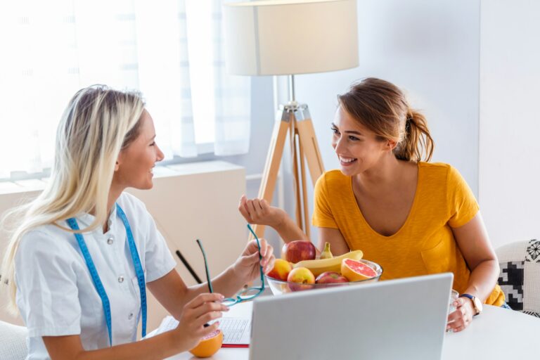Two women discussing recovery and wellness with fruit and a laptop.