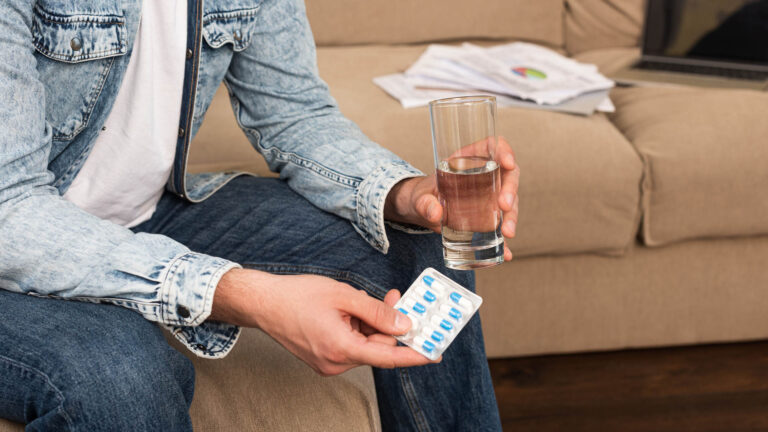 man holding blister with pills and glass of water