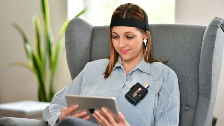 a woman sitting in a-chair using a tablet wearing neurofeedback