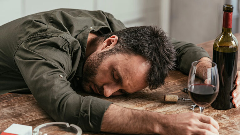 Drunk man sleeping on table with wine and cigarettes
