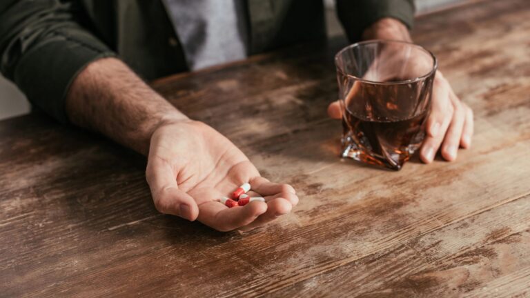 man holding whiskey glass and medicine in hands