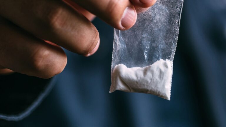 Mans hand holds plastic packet with cocaine powder