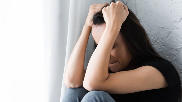 woman suffering from depression and crying while sitting by window