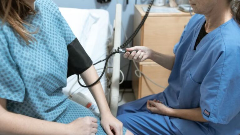 A nurse in blue scrubs checks the blood pressure