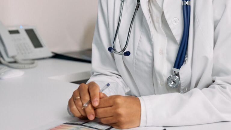 Doctor with stethoscope and white coat seated at a clinic desk